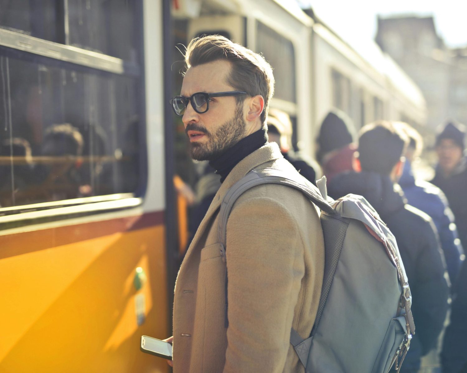 A stylish man with a backpack boards a tram in bustling Budapest, Hungary, during the day.